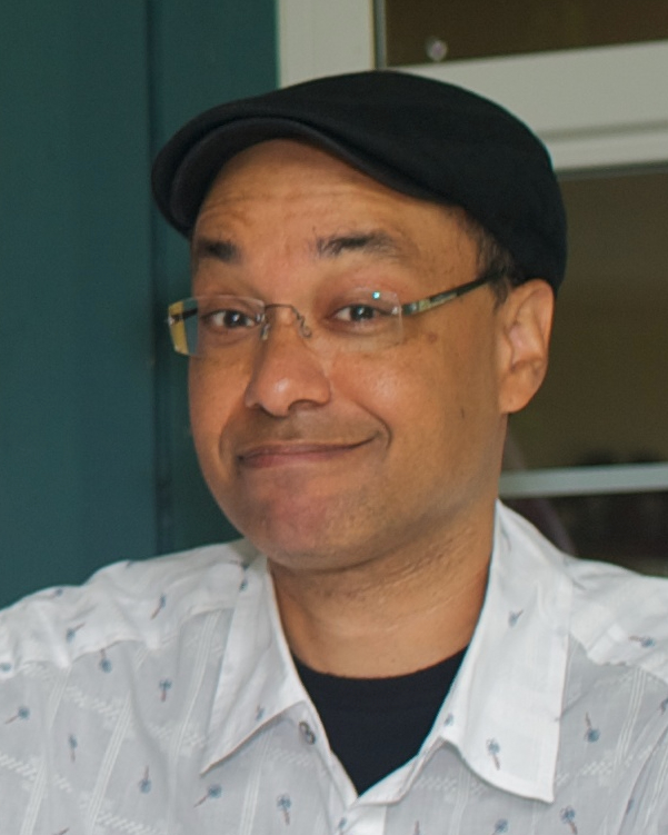 headshot portrait of smiling man with glasses and cap